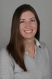 A headshot of Jessica Edmonds, a white woman smiling with brown hair, a gray sweater, with a gray background.